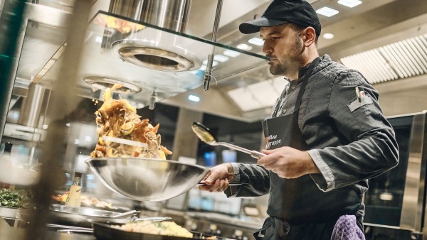 Koch-schwingt-Wok-Pfanne-an-Wok-Station-im-Betriebsrestaurant