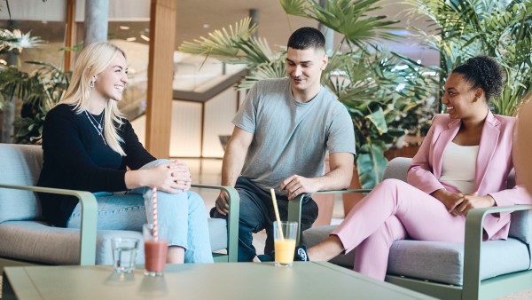 3-junge-Mitarbeiter-sitzen-in-Palmengarten-zusammen-und-trinken-Smoothies