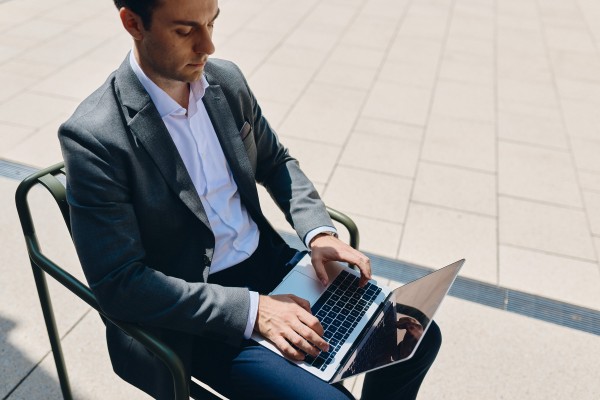 Junger Mann in Anzug arbeitet draußen am W&W-Campus mit seinem Laptop