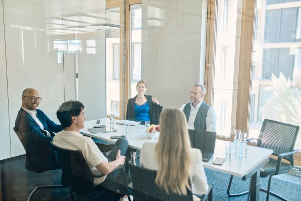Fünf Mitarbeiter haben eine Teambesprechung im hellen Besprechungsraum auf dem Campus
