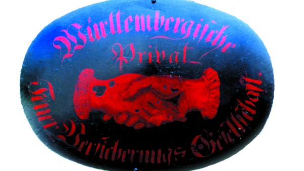 Schild der Gesellschaft: zwei rote, ineinander verschlungene Hände auf schwarzem Grund, Symbol des Gegenseitigkeitsvereins