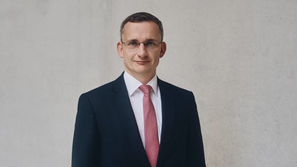 Portrait von Matthias Bogk, Chief Financial Officer, Chief Risk Officer und Vorstandsmitglied lächelt im Anzug vor grauer betonwand.