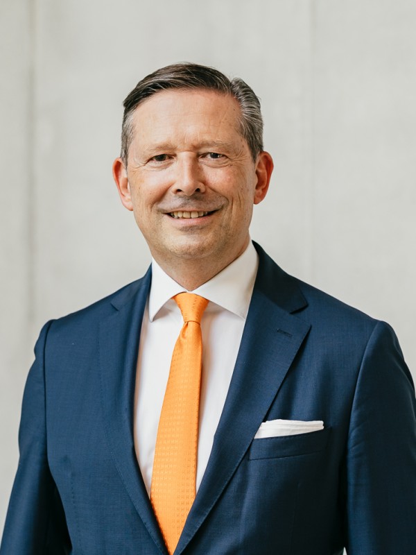 Vorstandsworsitzender Jürgen A. Junker steht vor einer grauen Betonwand