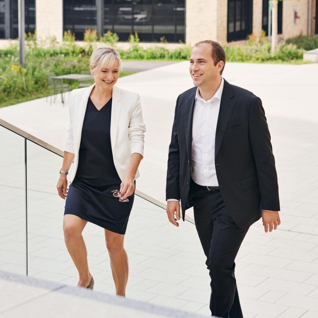 Frau und Mann im mittleren Alter laufen lächelnd eine Treppe am W&W-Campus hinauf