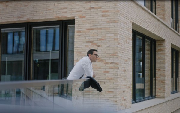 Mann lehnt sich auf das Geländer im Campus und schaut in die Ferne