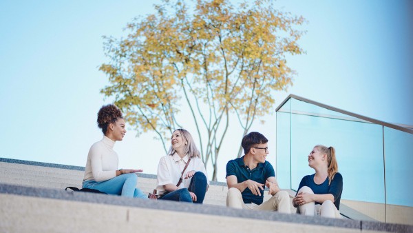 Vier junge Leute sitzen nebeneinander auf einer Treppe und unterhalten sich