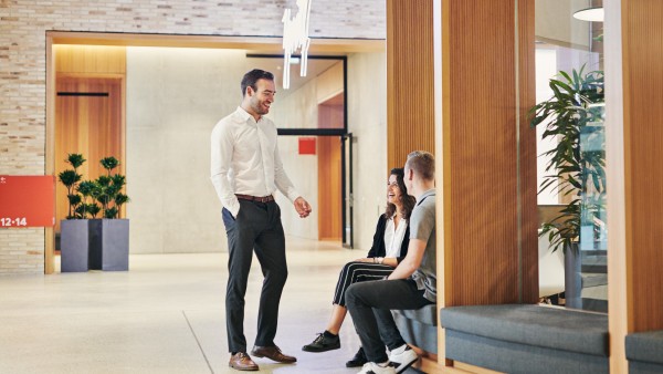 Junge Frau und Mann sitzen am Bistro und vor ihnen steht ein Mann und erklärt etwas
