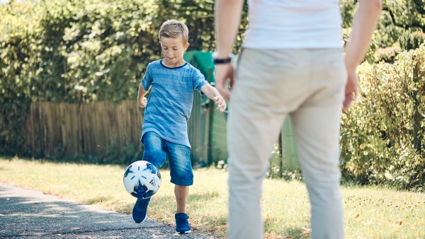 Kleiner Junge der mit einem Erwachsenen Fußball spielt
