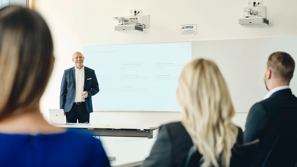 Ein älterer Mann hält vor drei jungen Menschen einen Seminarvortrag