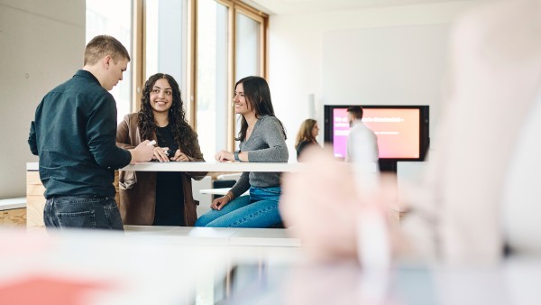 Drei-Azubis-befinden-sich-an-einem-Stehtisch-im-Kreativraum-und-unterhalten-sich