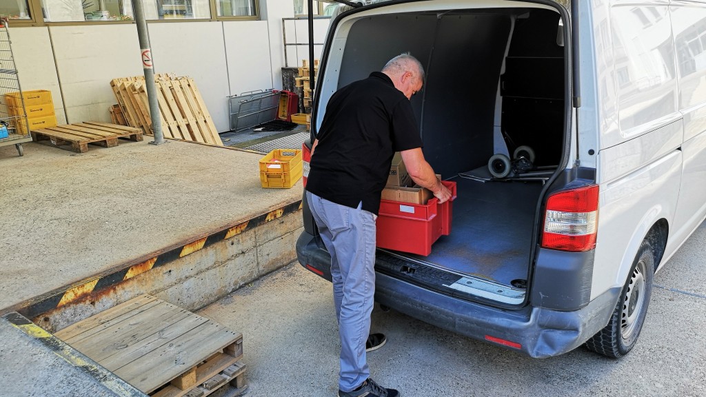 Mann hebt rote Kisten in grauen Transporter