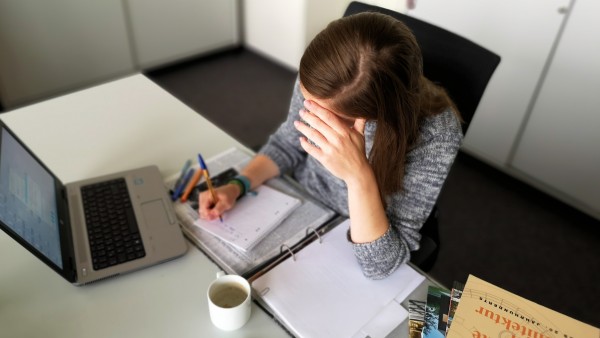junge Frau sitzt am Schreibtisch und hat ihren Kopf mit dem Arm gestützt