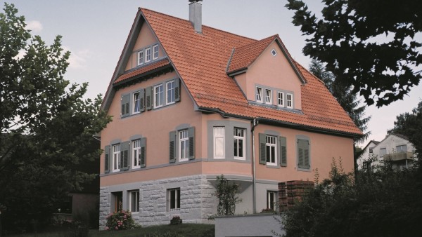 Hellrotes Haus mit Ziegeldach umgeben von Bäumen