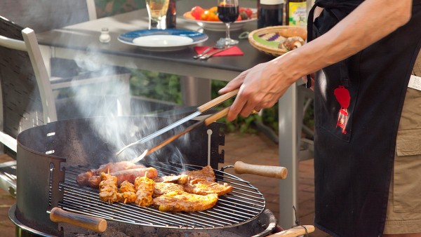 Kahler Mann mit Brille in Schürtze am Grill