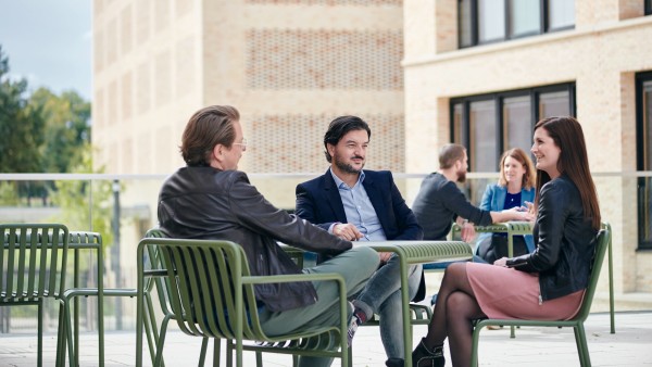 Fünf Mitarbeiter unterschiedlichen Alters sitzen draußen vor dem Campus und unterhalten sich