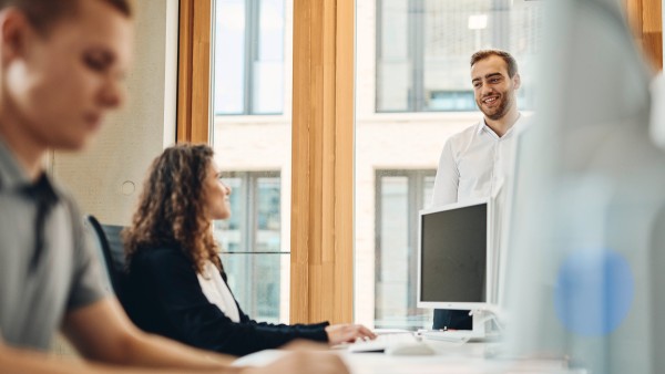 drei junge Mitarbeiter sitzen an ihrem Schreibtisch in einem modernen Großraumbüro und unterhalten sich