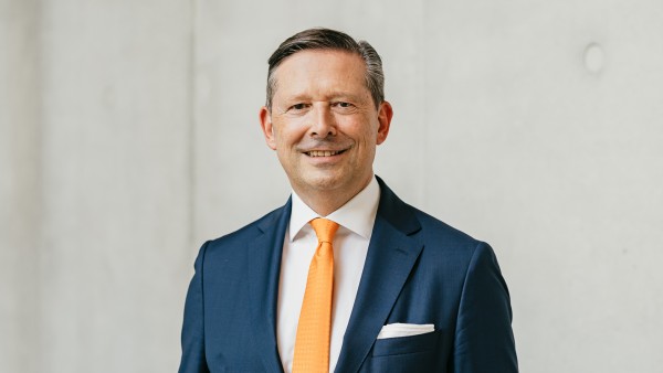 Vorstandsworsitzender Jürgen A. Junker steht vor einer grauen Betonwand