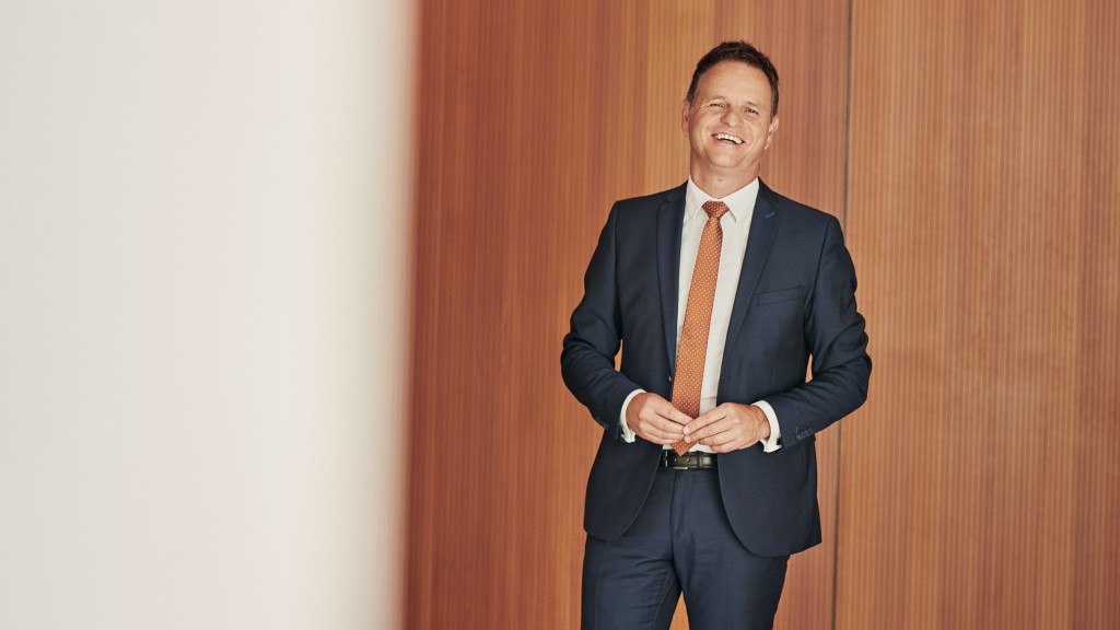 Ein lachender Mann im mittleren Alter der vor einer Holzwand steht